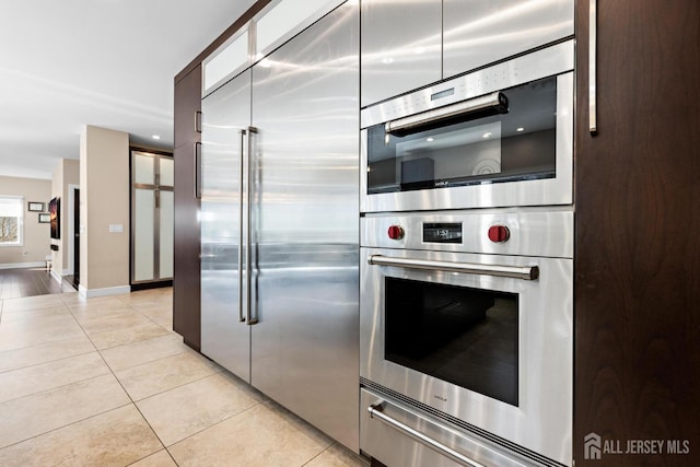 kitchen featuring light tile patterned floors, baseboards, stainless steel appliances, and a warming drawer