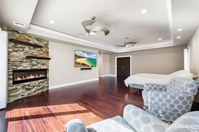 bedroom featuring dark wood-style flooring, a raised ceiling, visible vents, a large fireplace, and baseboards