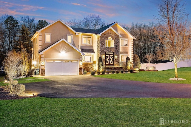 traditional-style house with aphalt driveway, stucco siding, fence, a garage, and stone siding