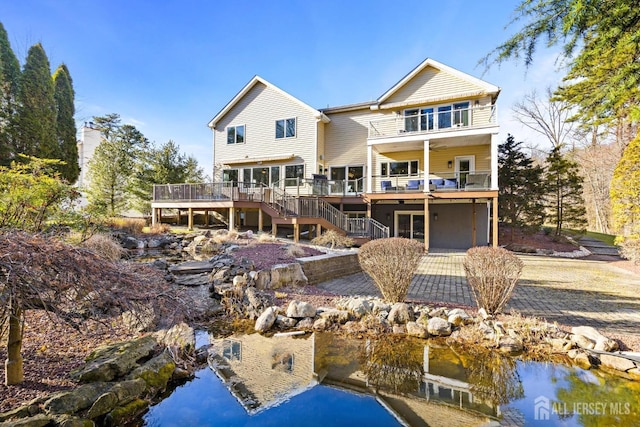 rear view of property with stairway, a balcony, and a deck