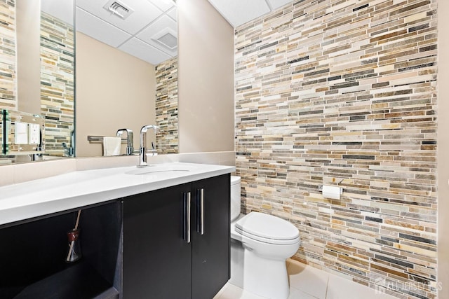 bathroom with a drop ceiling, toilet, visible vents, vanity, and tile patterned floors