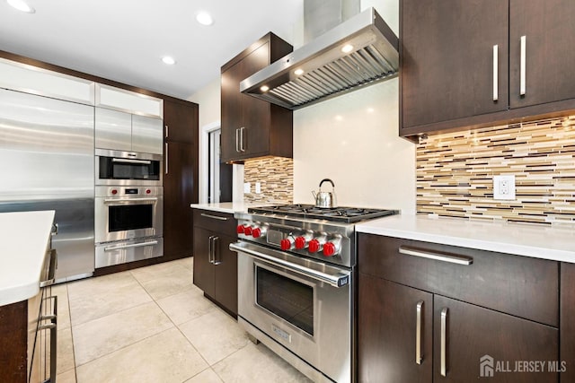 kitchen featuring stainless steel appliances, light countertops, wall chimney range hood, decorative backsplash, and a warming drawer