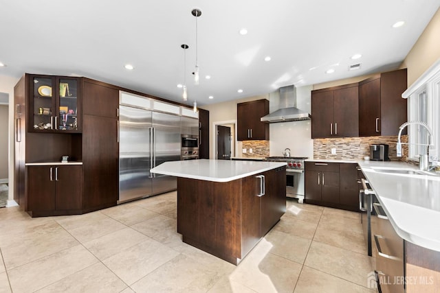 kitchen with light countertops, glass insert cabinets, a sink, wall chimney range hood, and high quality appliances