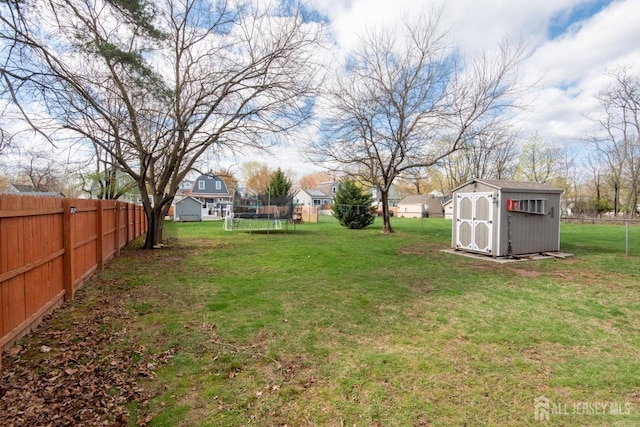 view of yard with a trampoline, a shed, a fenced backyard, and an outbuilding