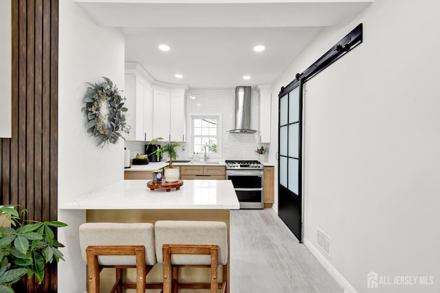 kitchen featuring wall chimney range hood, light countertops, a barn door, light wood-style floors, and double oven range