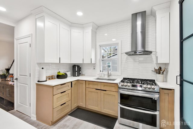 kitchen with wall chimney exhaust hood, a sink, light countertops, light wood-type flooring, and double oven range