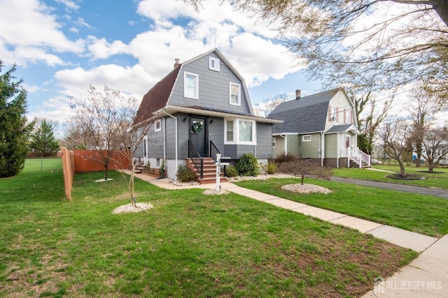 colonial inspired home with entry steps, a gambrel roof, fence, and a front lawn