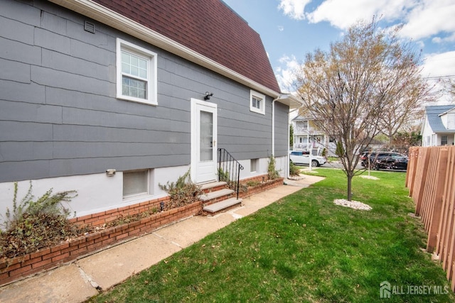 back of house featuring entry steps, a shingled roof, fence, and a lawn