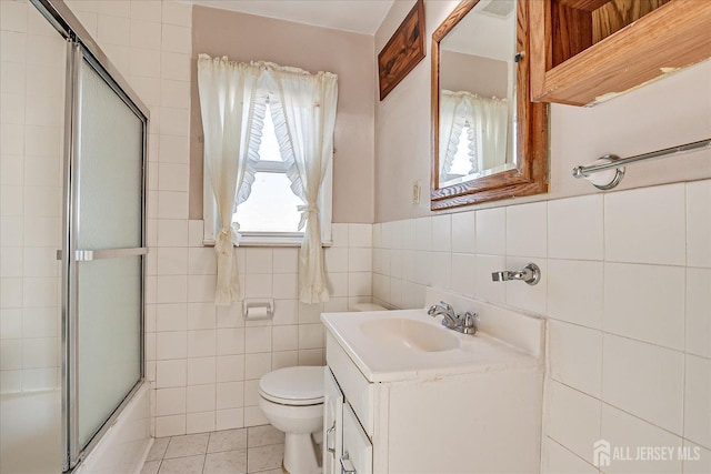 full bathroom with bath / shower combo with glass door, tile walls, tile patterned flooring, vanity, and toilet