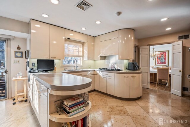 kitchen featuring tasteful backsplash, sink, stainless steel gas cooktop, kitchen peninsula, and a notable chandelier