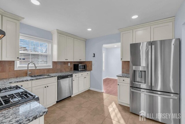 kitchen with stone counters, sink, tasteful backsplash, light tile patterned floors, and appliances with stainless steel finishes