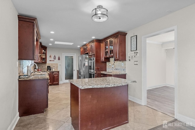 kitchen with light tile patterned floors, glass insert cabinets, freestanding refrigerator, a sink, and baseboards