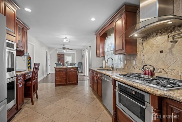 kitchen featuring light stone counters, tasteful backsplash, appliances with stainless steel finishes, a sink, and wall chimney range hood