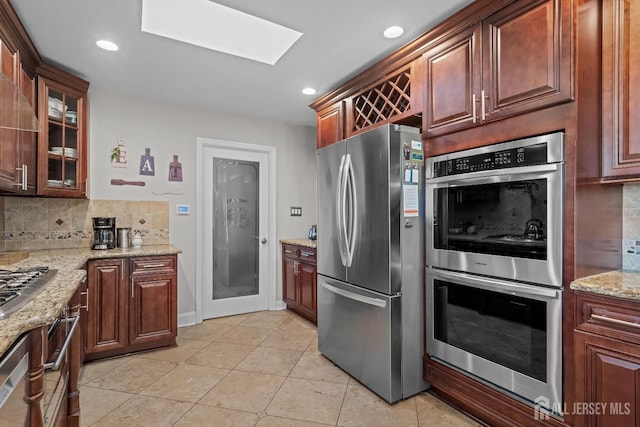 kitchen with light tile patterned floors, decorative backsplash, glass insert cabinets, light stone countertops, and stainless steel appliances