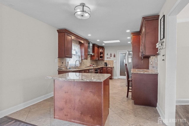 kitchen featuring wall chimney range hood, backsplash, a sink, and light stone counters