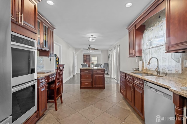 kitchen with decorative backsplash, appliances with stainless steel finishes, a sink, ceiling fan, and light stone countertops