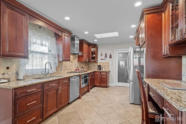 kitchen featuring a skylight, a sink, stainless steel appliances, wall chimney range hood, and backsplash