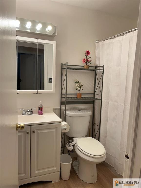 bathroom featuring wood finished floors, toilet, a shower with shower curtain, and vanity