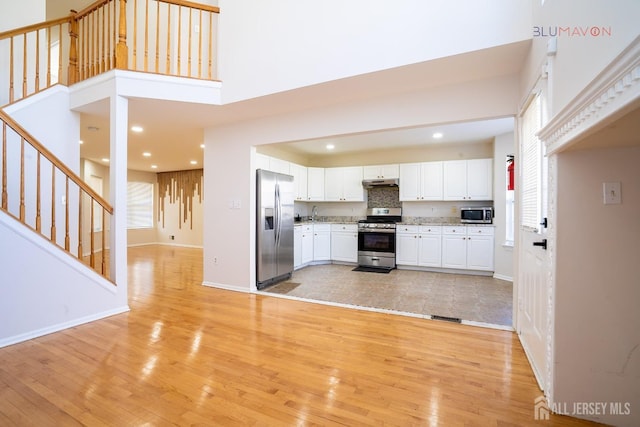 kitchen with a high ceiling, white cabinetry, stainless steel appliances, decorative backsplash, and light wood-type flooring