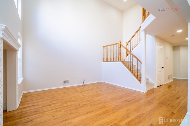 unfurnished living room with light hardwood / wood-style floors and a towering ceiling