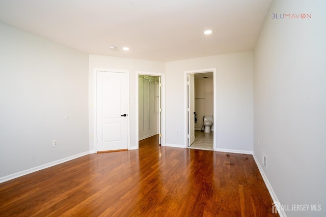 unfurnished bedroom featuring a spacious closet, connected bathroom, and hardwood / wood-style floors