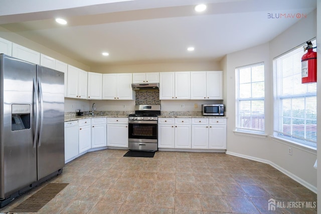 kitchen with appliances with stainless steel finishes, sink, white cabinets, and light stone countertops