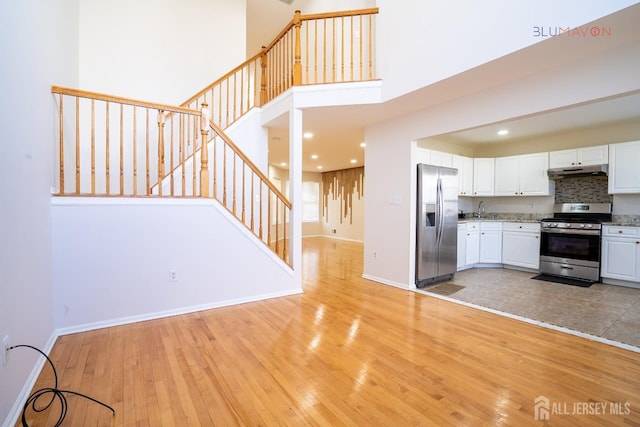 kitchen with appliances with stainless steel finishes, decorative backsplash, white cabinets, light hardwood / wood-style flooring, and sink