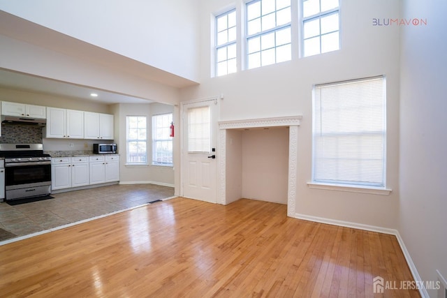 kitchen with white cabinets, a towering ceiling, stainless steel appliances, and light hardwood / wood-style flooring