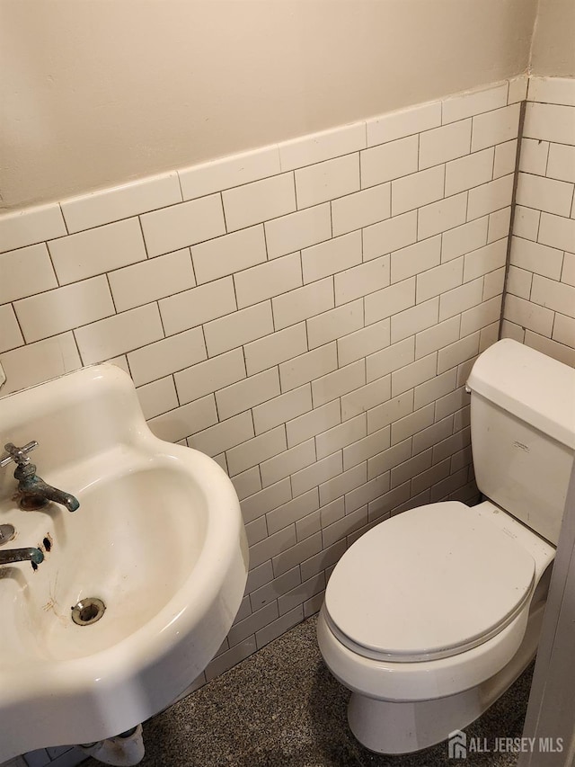 bathroom featuring toilet, sink, and tile walls