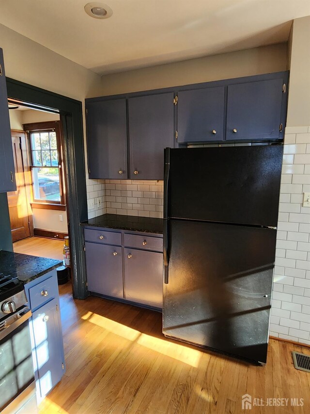 kitchen with light wood-type flooring, tasteful backsplash, black fridge, and dark stone countertops