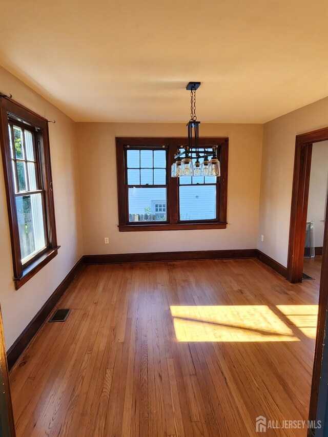 unfurnished dining area with light wood-type flooring and an inviting chandelier