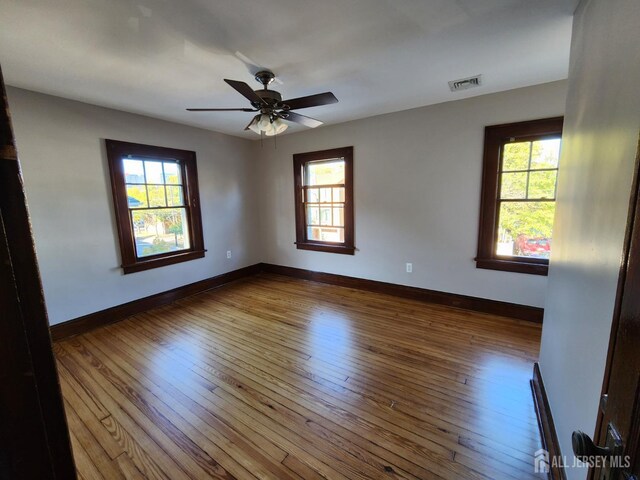 empty room with hardwood / wood-style flooring, ceiling fan, and a healthy amount of sunlight