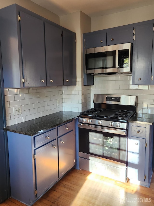 kitchen with backsplash, light hardwood / wood-style floors, dark stone counters, and appliances with stainless steel finishes