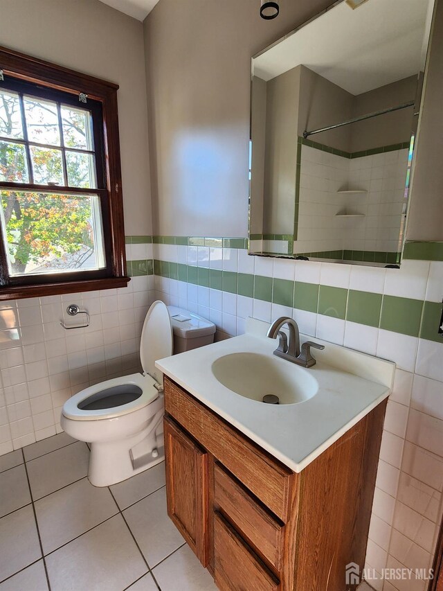 bathroom featuring vanity, tile patterned flooring, toilet, tiled shower, and tile walls