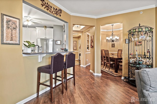 kitchen with a breakfast bar, dark wood finished floors, white cabinetry, freestanding refrigerator, and crown molding