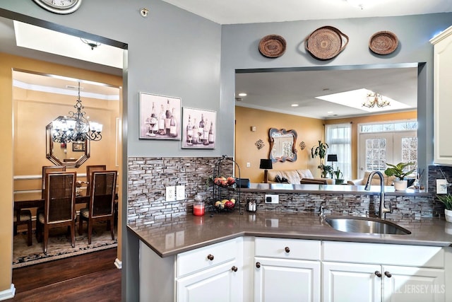 kitchen with dark countertops, decorative backsplash, dark wood-style floors, a notable chandelier, and a sink