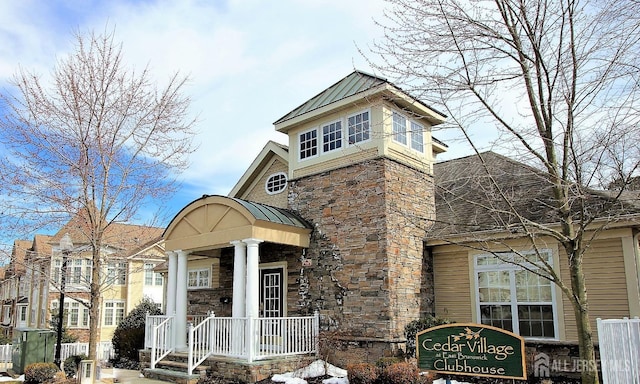 view of front of house with a standing seam roof, fence, stone siding, and metal roof