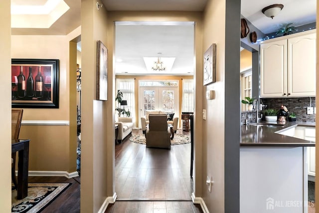 hallway featuring a sink, baseboards, an inviting chandelier, and wood finished floors