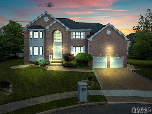 view of front facade with an attached garage, a yard, decorative driveway, and brick siding