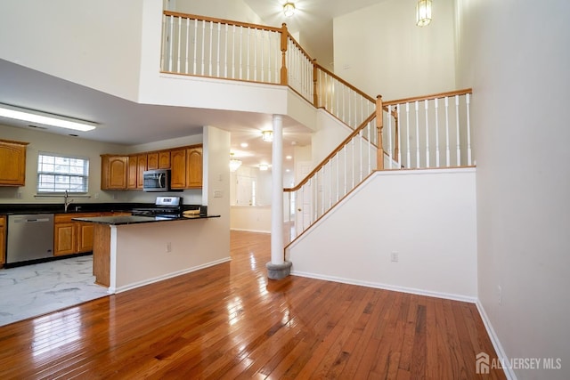 kitchen with hardwood / wood-style flooring, a towering ceiling, kitchen peninsula, and appliances with stainless steel finishes