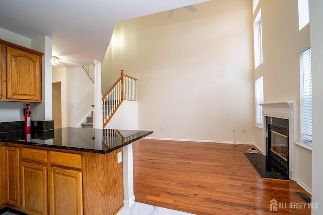 kitchen featuring a fireplace, kitchen peninsula, light hardwood / wood-style flooring, and dark stone countertops