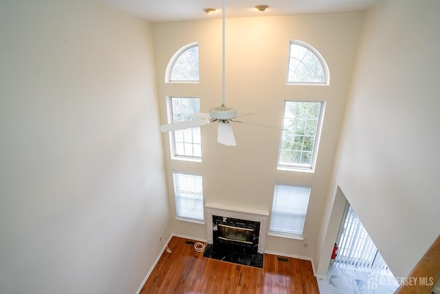 living room with hardwood / wood-style flooring, a towering ceiling, a premium fireplace, and ceiling fan