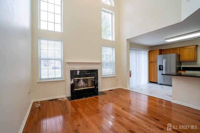 unfurnished living room with a premium fireplace, a towering ceiling, and light hardwood / wood-style flooring