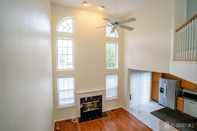 living room featuring light wood-type flooring, a high end fireplace, ceiling fan, and a high ceiling