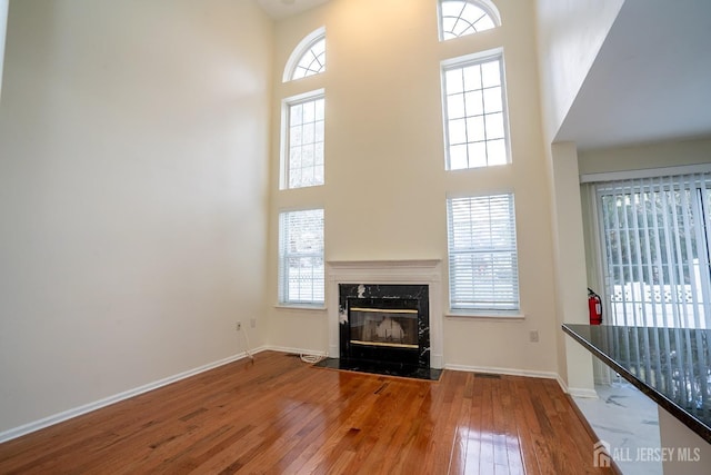 unfurnished living room featuring a towering ceiling, wood-type flooring, and a premium fireplace