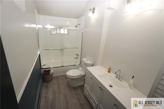 bathroom with wood finished floors, toilet, combined bath / shower with glass door, and vanity