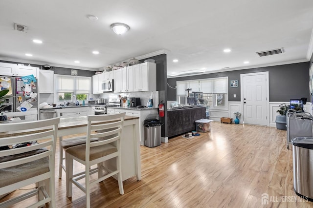 kitchen with stainless steel appliances, a wainscoted wall, visible vents, white cabinetry, and ornamental molding