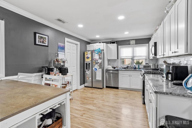 kitchen with light wood finished floors, visible vents, white cabinetry, ornamental molding, and appliances with stainless steel finishes