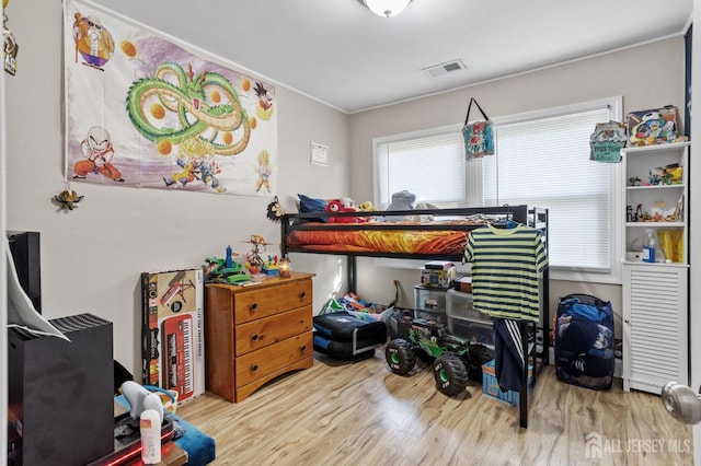 bedroom with wood finished floors, visible vents, and ornamental molding