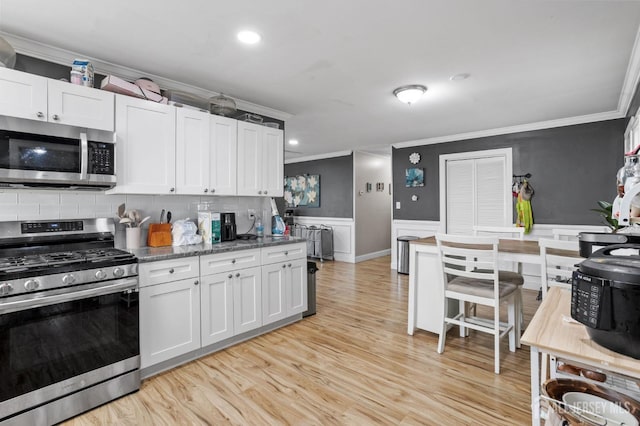 kitchen featuring tasteful backsplash, crown molding, light wood-style flooring, appliances with stainless steel finishes, and wainscoting